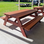 A frame hardwood picnic table on a concrete surface with grass and vehicles in the background