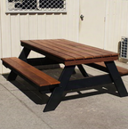 A frame picnic table with painted black frame with jarrah table top on concrete with a building in the background.
