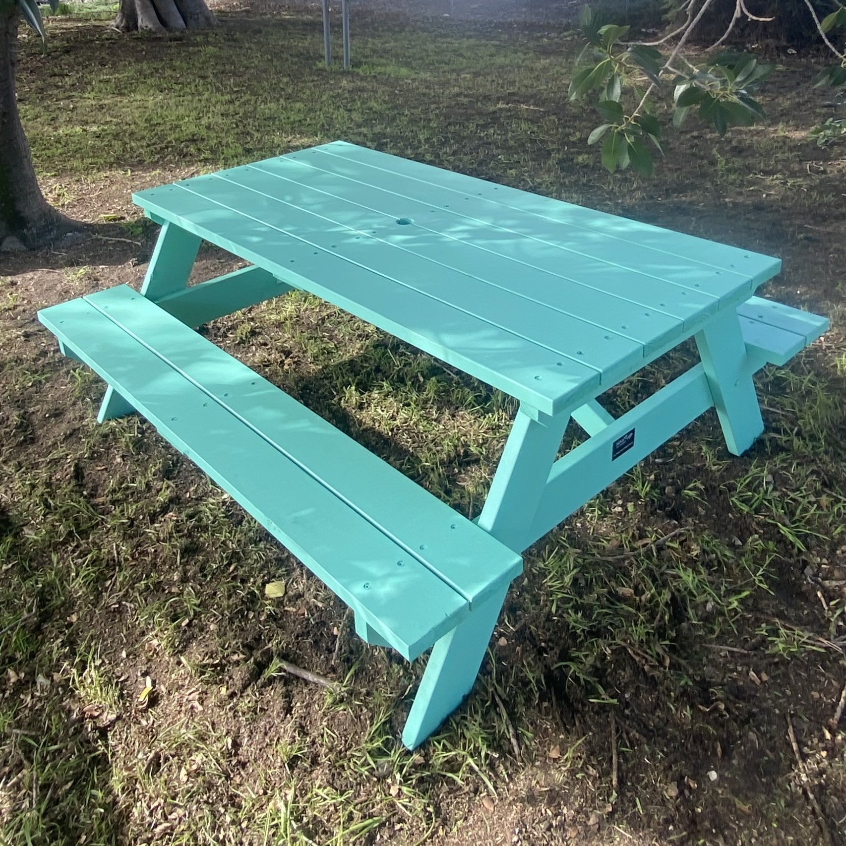 A mint green painted wooden picnic table with attached benches, shown outdoors on grassy ground near trees.