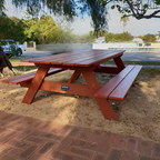 Hardwood picnic table in a park setting with trees and a building in the background.