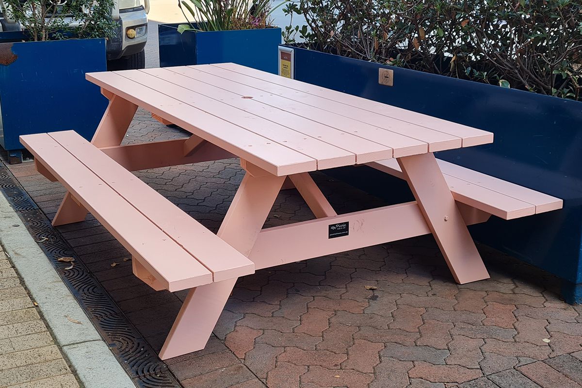 Pink A frame Pine picnic table with attached benches on a paved area