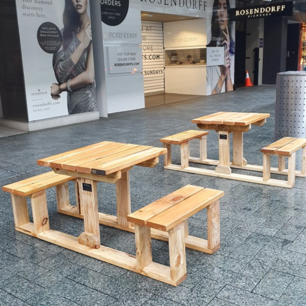 Wooden U Shape 2 seater outdoor tables on a pavement with shopping center in the background